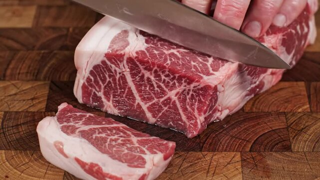 Chef carefully slicing a thick cut of raw meat with a large carving knife on a wooden cutting board for a delicious meal.