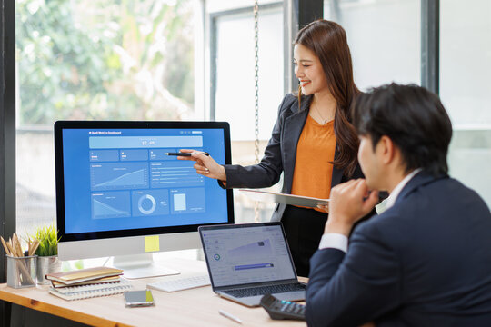 Two Business Professionals Analyzing Financial Dashboard in Modern Office pointing at data charts on a computer screen and collaborating in a modern office meeting.
