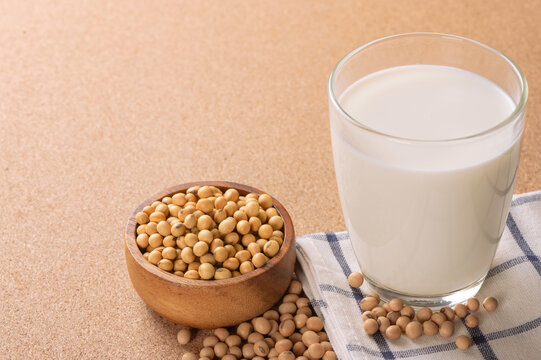 Glass of nutritious white soy milk served with organic soybeans in wooden bowl on brown background. Healthy plant-based protein drink and dairy alternative for wellness lifestyle.