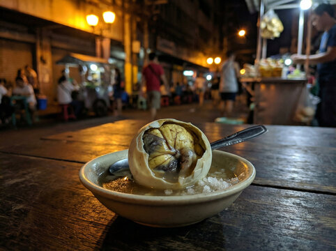Filipino Balut Fertilized Duck Egg Cracked Open with Broth and Salt on Dark Background No Face No Logo in Warm Manila Street Light