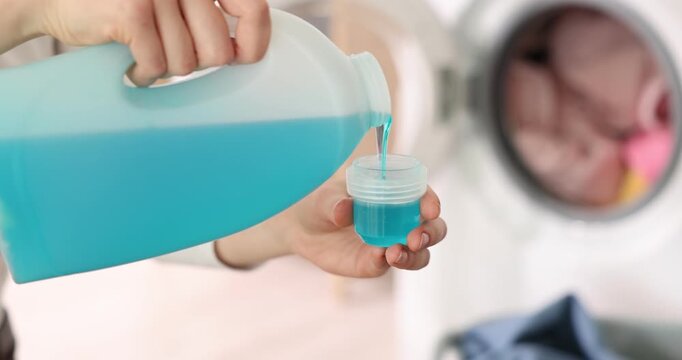 Woman pouring detergent into cap indoors, closeup. Laundry day