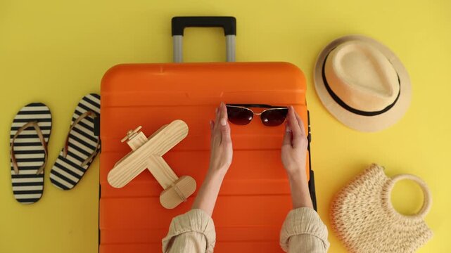 Woman with belongings and orange suitcase on yellow background, top view