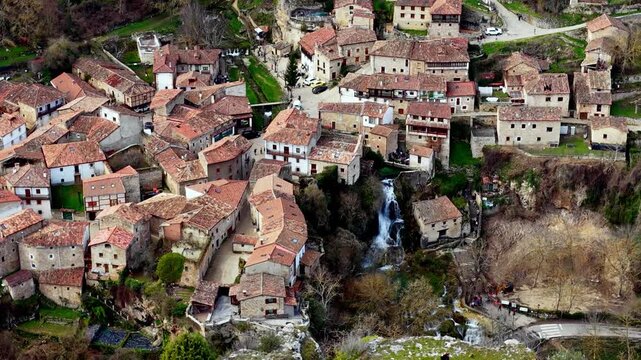 Vista a&eacute;rea cinematogr&aacute;fica de un pintoresco pueblo medieval enclavado en un paisaje rocoso del norte de Espa&ntilde;a, capturada con dron y zoom desde la distancia. Las casas de piedra se integran de forma 