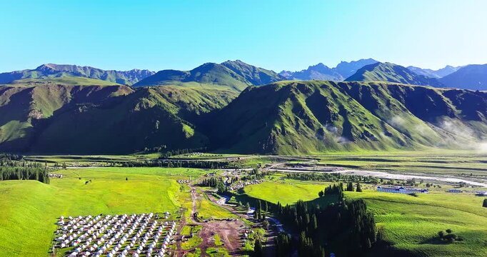 Aerial view of lush green mountain valley with camping tents and nomadic yurts, Xinjiang, China.