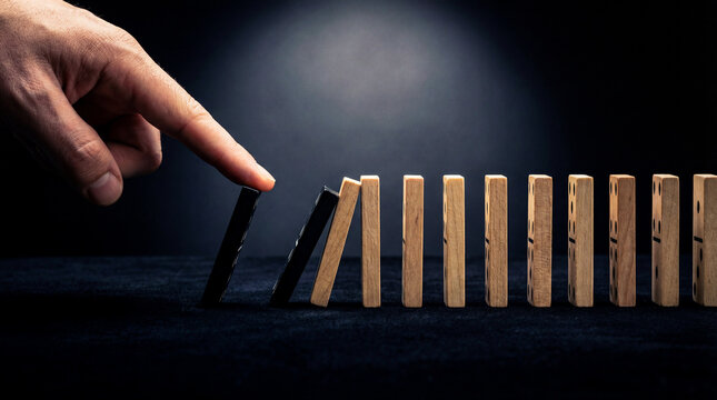 Finger pushing first domino in chain reaction, domino effect concept. Cause and consequence metaphor for business strategy, risk management and leadership decision.