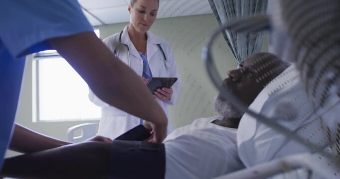 Nurse placing BP cuff on male patient, adjusting for medical monitoring while doctor using tablet