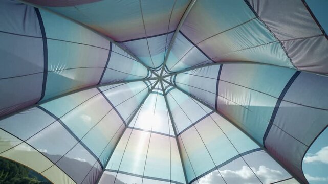 Canopy responding to wind and sun, tightening ribs and revealing shimmering seams in outdoor design