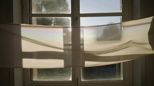 Billowing cloth being lifted by breeze across 4-pane window mullions at home, shifting light bands