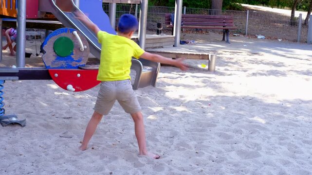 young boy in yellow t-shirt performing cartwheel on sandy playground, child's playful acrobatics expressive energy, handstands freedom, coordination, active childhood play, urban setting with slide