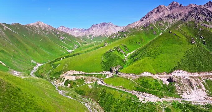 Aerial view of a winding road on steep green mountain slopes, Xinjiang, China.