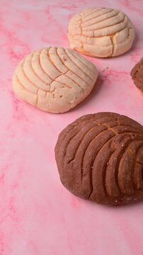 Aerial view of colorful Mexican bread on pink texture, Conchas of chocolate and vanilla