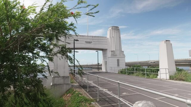 Looking at the old bridge archway with the new bridge passing behind. A plant sways in the wind in the foreground.