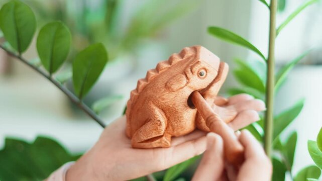 Guiro Money Toad. Hand holding wooden frog percussion instrument. Traditional guiro sound maker, handmade craft. Statue made from single piece wood. Stick back of toad, it will bring money