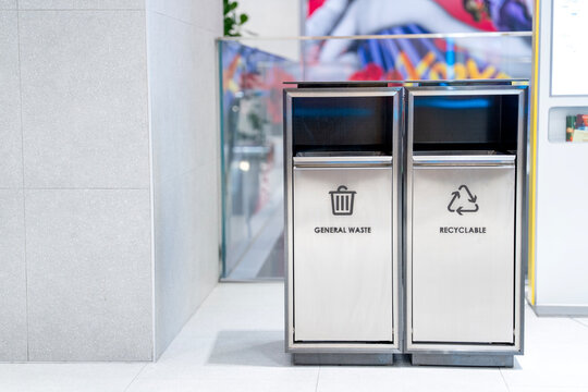 Modern stainless steel waste separation bins in a clean public indoor setting. Two metal containers labeled for general waste and recyclable materials promote environmental sustainability.