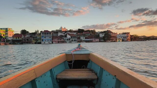 Boat travel on the Peten Itza lake in Flores, Guatemala. Nature and buildings in the background.  Calm river water and orange sunset . Colorful yellow and blue boat