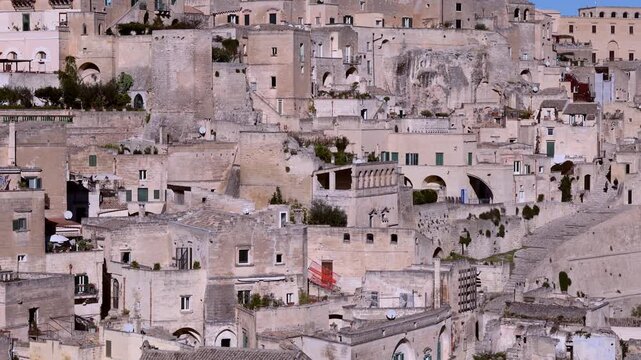 panoramic view of matera, italy, featuring ancient sassi limestone buildings and the iconic cathedral bell tower under a clear blue sky, capturing historic charm