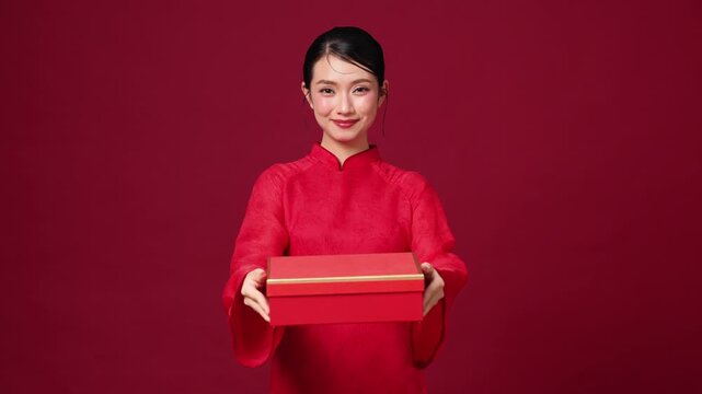 Asian woman holding red gift box, warm smile, festive outfit, ideal for holiday gift promotion visuals. Copy space