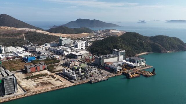 Stunning aerial view of tseung kwan o industrial estate between green hills and turquoise sea, showcasing modern waterfront infrastructure, business parks and coastal development