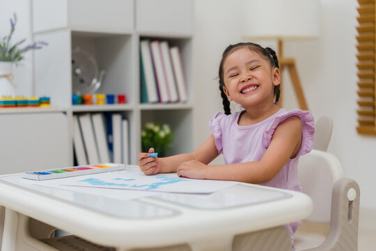 happy preschool child girl drawing and painting with colorful oil pastels on paper