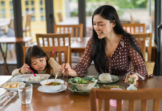 woman and preschool child girl eating with food together in restaurant