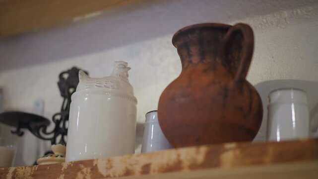 Terracotta pitcher on kitchen shelf, enamel jar and iron trivet nearby, textured clay surface in warm afternoon light, home cook imagined fetching water, rustic farmhouse mood, natural earth tones