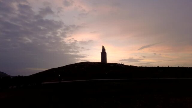 Stunning timelapse view of the tower of hercules in a coru&ntilde;a, spain, silhouetted against a beautiful sunset sky as the last light of day fades into twilight and the clouds move across the horizon