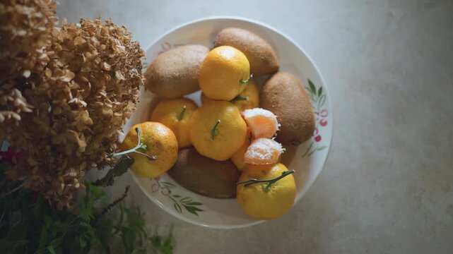 Rustic fruit bowl on kitchen counter, dried flowers and ripe mandarins nestled with kiwis under warm afternoon light, overhead frame evoking calm home cook centerpiece and seasonal comfort