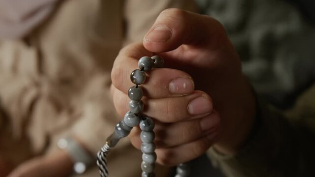Cinematic detail shot hand of unrecognizable Muslim man holding prayer beads and counting stones slowly following traditional rituals, copy space