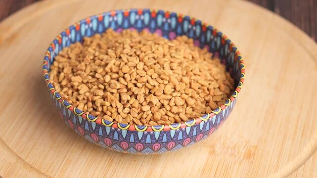 Fenugreek seeds in a colorful bowl, slowly rotating on a wooden surface, cinematic close-up.