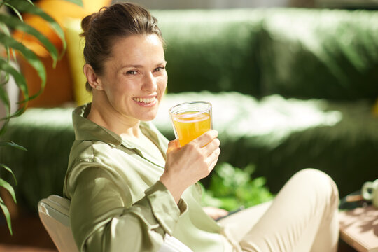 A smiling woman sits comfortably in her living room, enjoying a glass of orange juice as part of her healthy morning habits and relaxed home lifestyle.