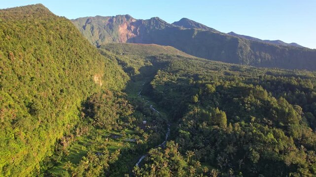 Aerial drone footage of Galunggung volcano mountain, at early sunrise, from Citiis hot spring area, with a wild river passing, wild forest, in Tasikmalaya regency, Java island, Indonesia