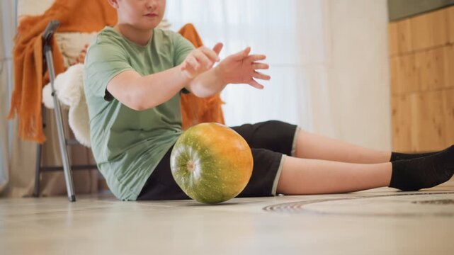 White boy sits on floor with squash, kitchen corner with cozy chair and orange throw, child touches bumpy skin and studies weight, hands exploring produce like small kitchen helper preparing