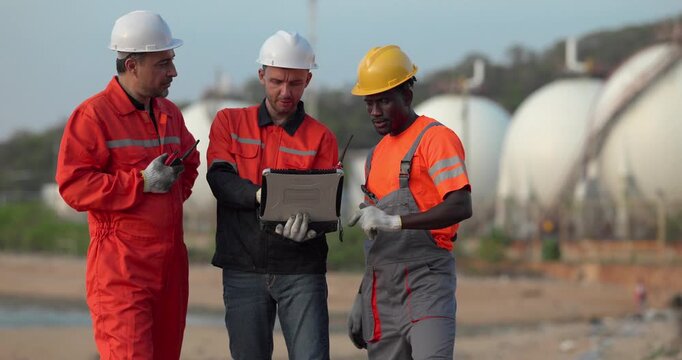 Industrial workers and engineers review refinery operations near storage tanks in daylight, illustrating fuel supply risk, market volatility, and economic uncertainty.
