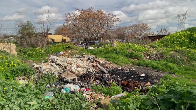 Neglected landscape featuring an illegal garbage dump, discarded waste materials, and burned residue, highlighting environmental pollution and abandonment