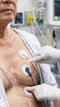 Technician adjusting cardiac monitoring electrodes on senior ecg patient in hospital room