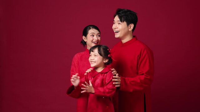 Asian couple with child between them, smiling and clapping, family-focused New Year theme