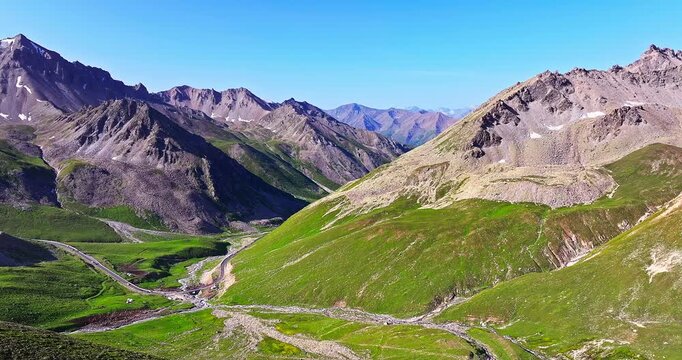 Aerial view of a winding road through a rugged high-mountain valley under a clear blue sky, Xinjiang, China.