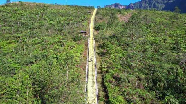 Aerial drone footage of someone alone climbing the Galunggung volcano mountain yellow giant stairs, at early sunrise, with forests around, in Tasikmalaya regency, Java island, Indonesia