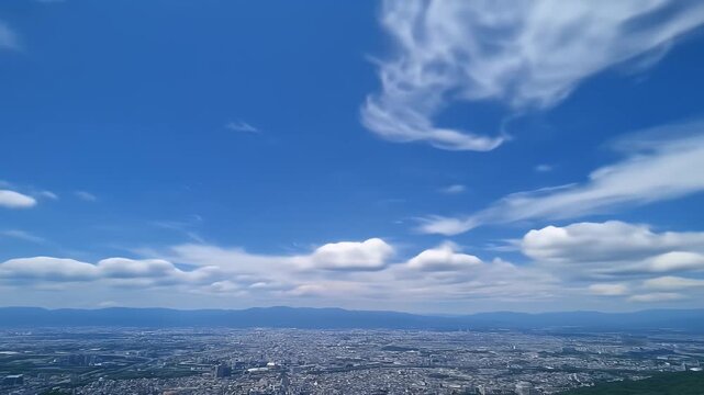 Panoramic view of a city nestled between mountains, a vibrant blue sky dotted with fluffy white clouds
