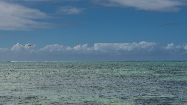 Endless turquoise ocean. Ripples on the water. A multicolored parachute is flying over the sea, against a background of blue sky and clouds. Mauritius.  &Icirc;le aux Cerfs
