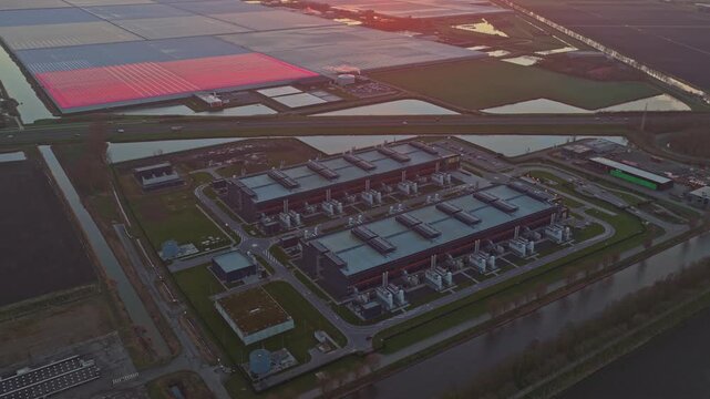 High angle aerial footage of a large data center complex surrounded by water and countryside. The sunrise illuminates the modern architecture