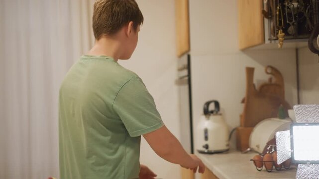 Youth cooking scene. Young male preparing family dinner. Boy in casual shirt gathering ingredients in warm kitchen. Young teenage boy focusing on preparing meal in cozy domestic setting