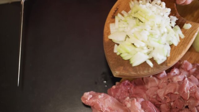 Chopping raw meat. Preparing diced onions and meat. Closeup of onion and meat preparation under warm lighting. Hands expertly chopping diced onion and raw meat on wooden board in cozy kitchen