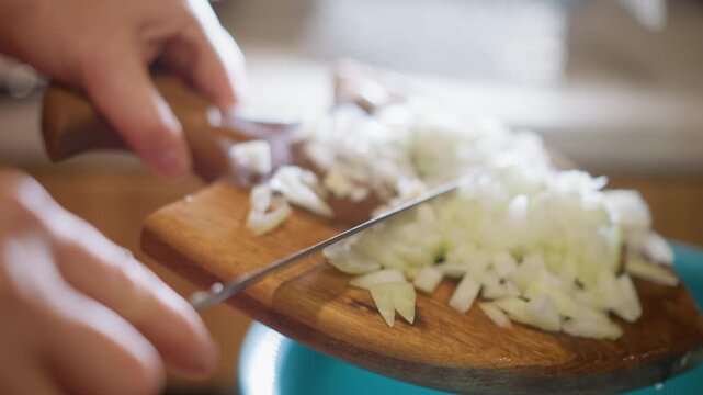 Closeup of chopping onion. Preparing kitchen with onion scraps into container in natural light. Closeup of person transferring onion pieces from cutting board to bowl under natural lighting