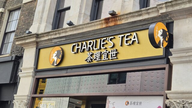 London UK 02.07.2025 charlies tea shop storefront with bright yellow sign and asian lettering on historic building facade urban street food and beverage concept