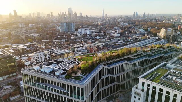 A back aerial view of a commercial building complex with the sun rising over the London skyline.