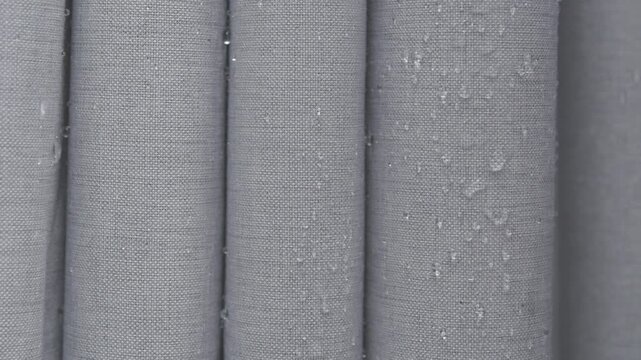 Water droplets slide off gray water repellent fabric in closeup, showing waterproof textile surface and moisture resistance