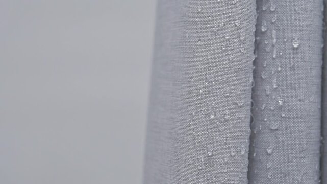 Water beads on gray shower curtain in closeup, showing water repellent fabric texture and waterproof bathroom material