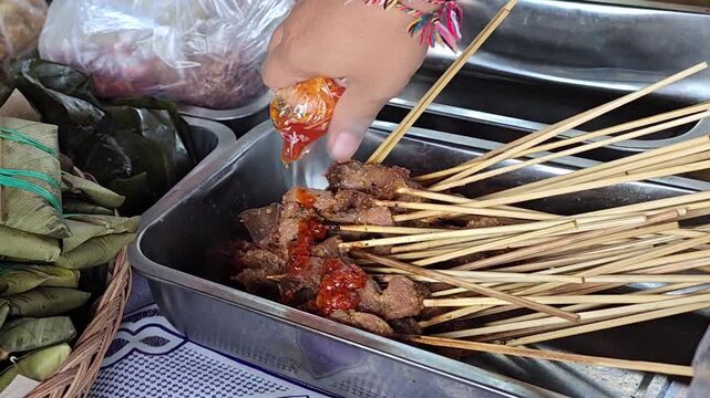 Adding spicy red sambal sauce to traditional beef sate skewers in Indonesia