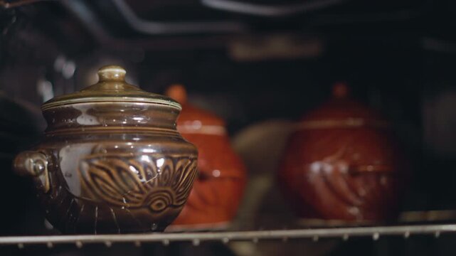 Clay pots baking in oven, warm glow. Close shot of ceramic pots on oven rack, rustic glaze catching light, slow braise or casserole cooking, cozy kitchen atmosphere, evening meal prep